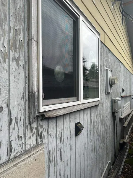 Exterior view of weathered wooden siding with peeling paint and a window