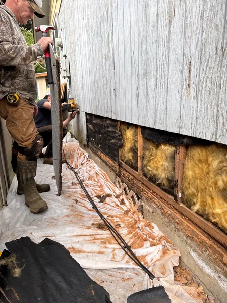 Worker using hydraulic jack to lift and repair sagging foundation beam under house