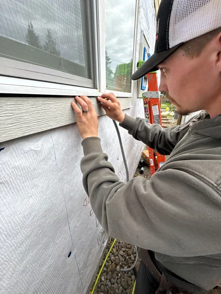 Worker installing white siding below window with precision