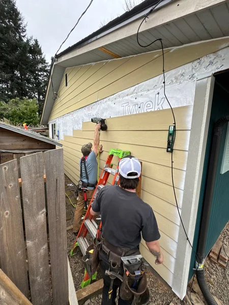 Two workers installing or removing house siding on exterior wall