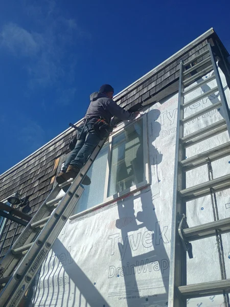Worker on ladder installing or repairing exterior siding on house wall