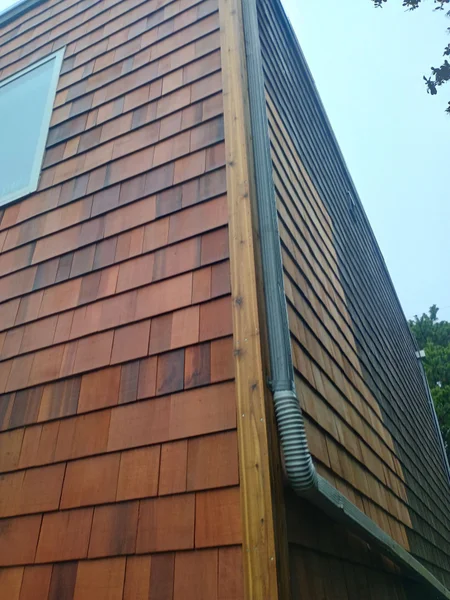 Cedar shake siding installation on building exterior corner with downspout