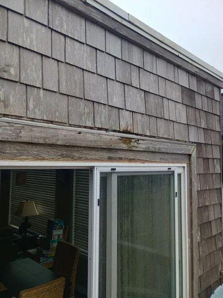 Weathered cedar shake siding exterior showing aging and potential dry rot damage above sliding door
